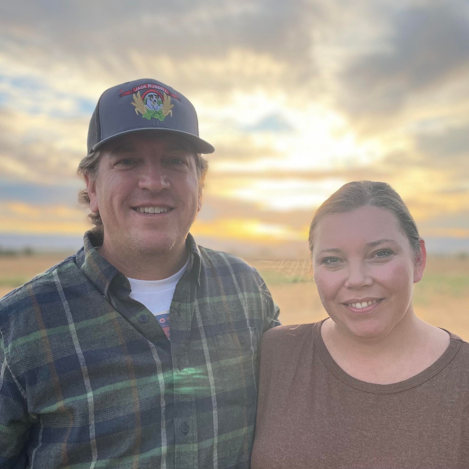 A man and a woman are posing for a picture in a field at sunset.