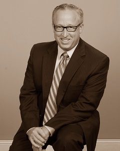 Mike Williams in a suit and tie is sitting on a chair .