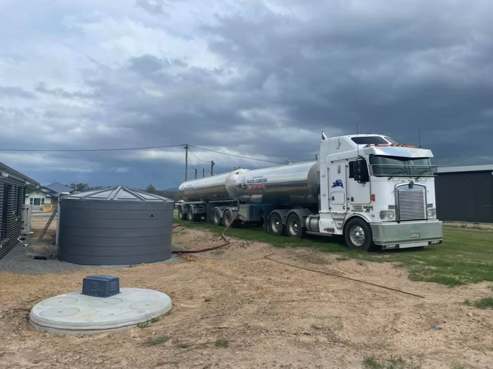A White Semi Truck Is Parked in A Dirt Field Next to A Water Tank — Stolzenberg Water Carriers in Gympie, QLD