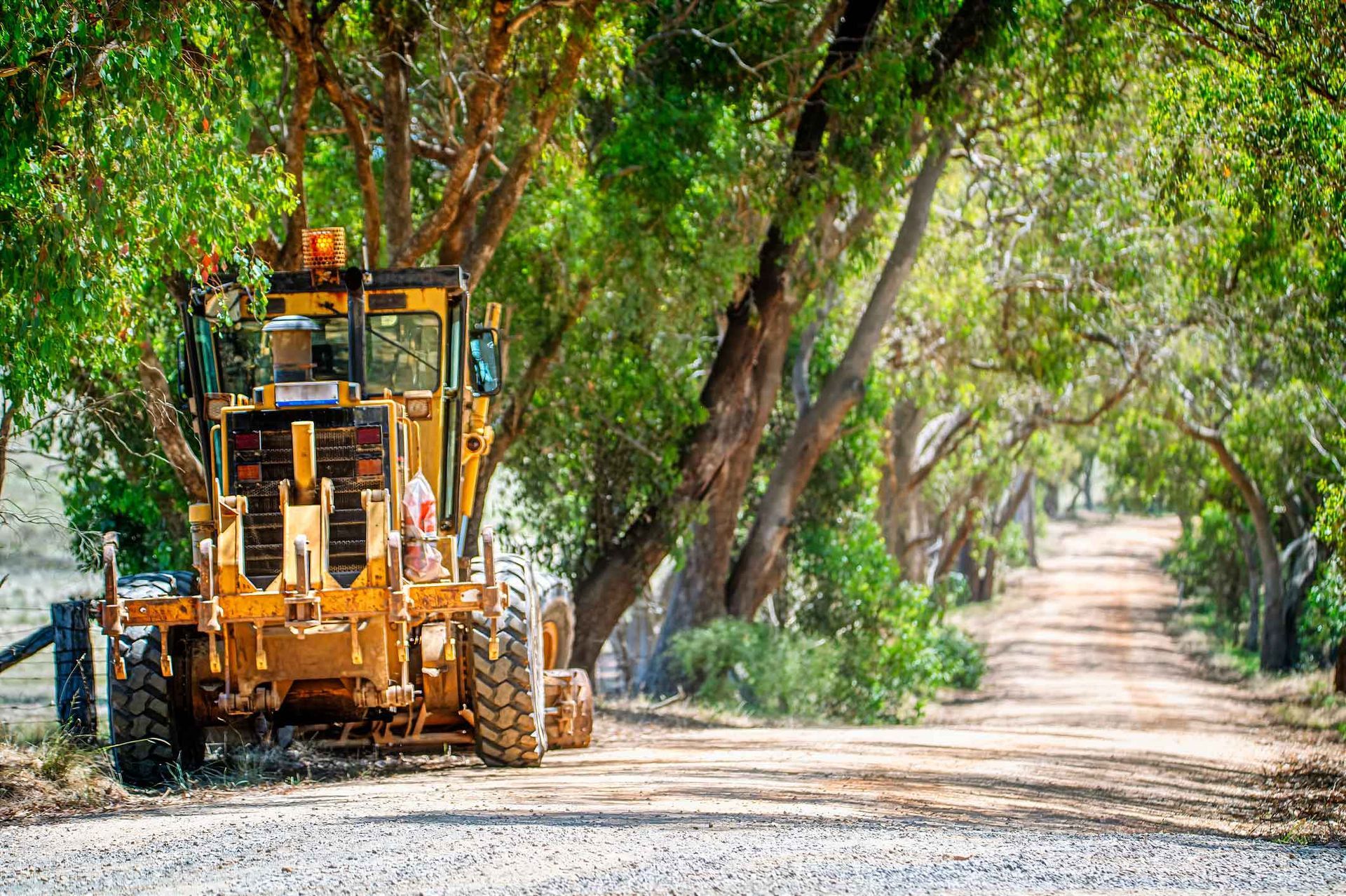 A Bulldozer Is Driving Down A Dirt Road Surrounded By Trees – Port Pirie, SA - Flinders Earthmoving & Blue Metal Supplies