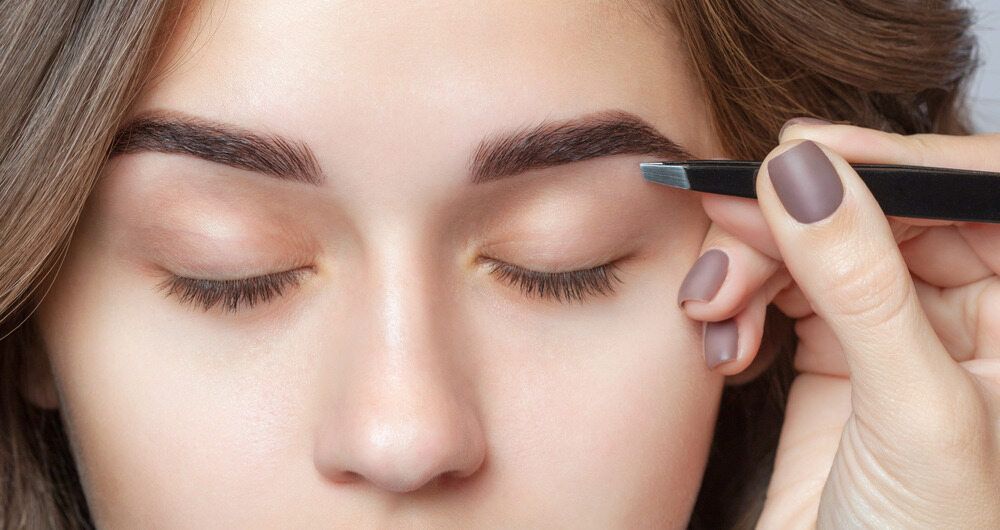 A Woman is Plucking Her Eyebrows With a Tweezer — Southside Hair & Beauty Design In South Tamworth, NSW
