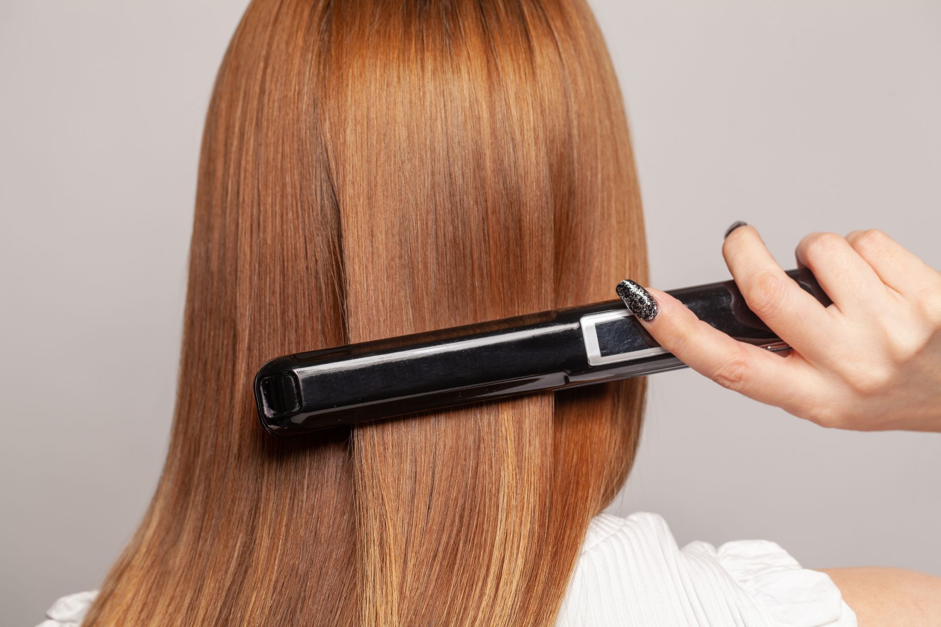Person Straightening Reddish-brown Hair With a Black Flat Iron — Southside Hair & Beauty Design In South Tamworth, NSW
