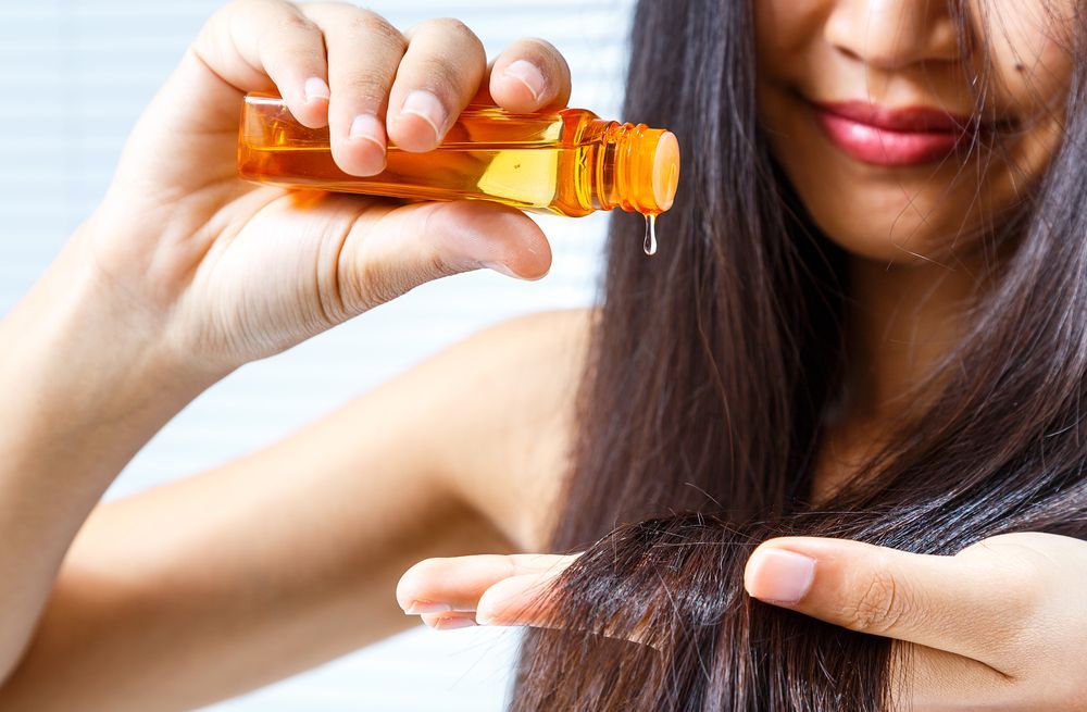 Person Applying Oil to Dark Hair From a Small Orange Bottle — Southside Hair & Beauty Design In South Tamworth, NSW