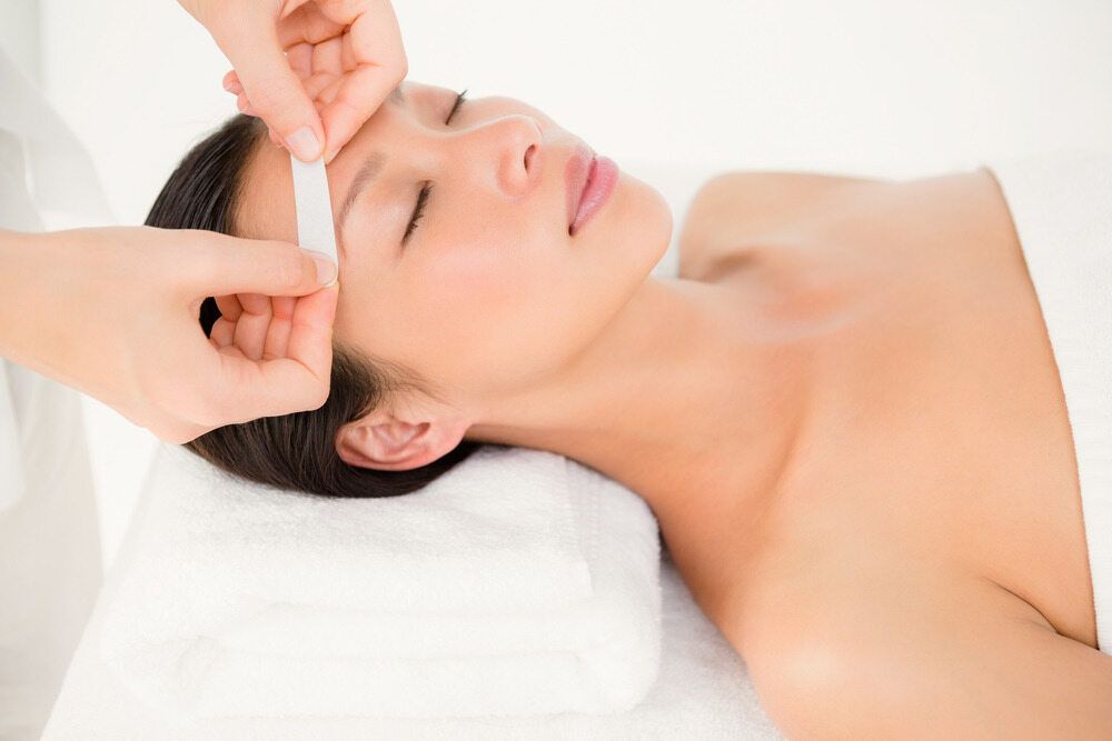 Woman Getting Her Eyebrow Waxed at a Spa, Laying on a White Towel — Southside Hair & Beauty Design In South Tamworth, NSW