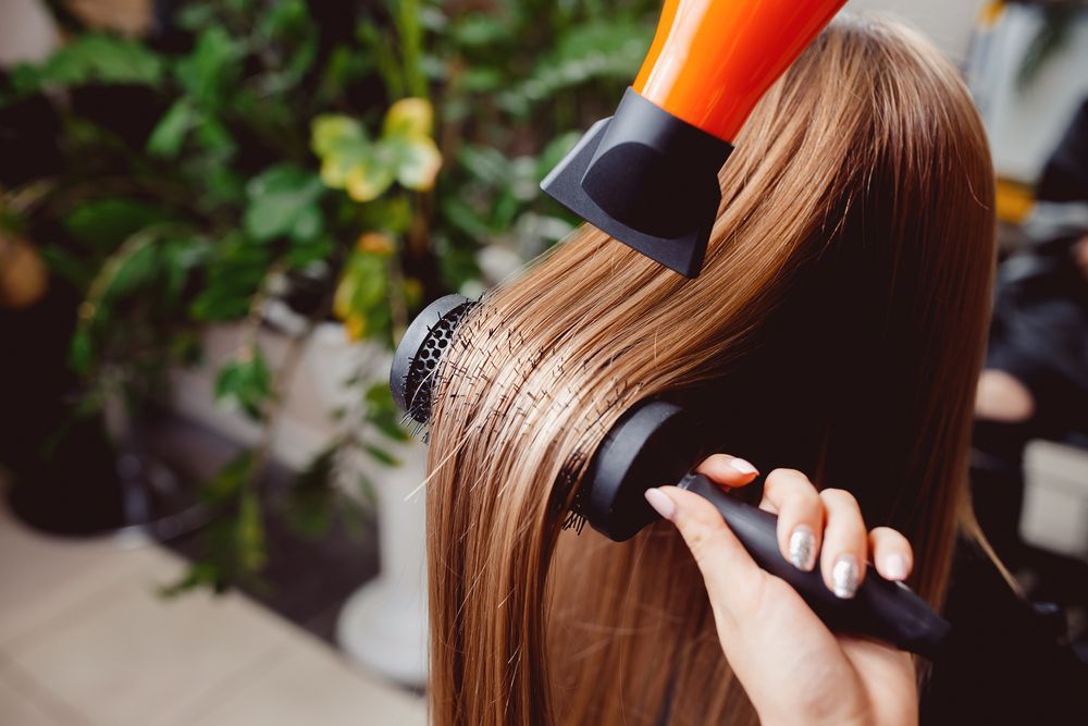 Hair being styled with a round brush and orange hairdryer in a salon — Southside Hair & Beauty Design In South Tamworth, NSW