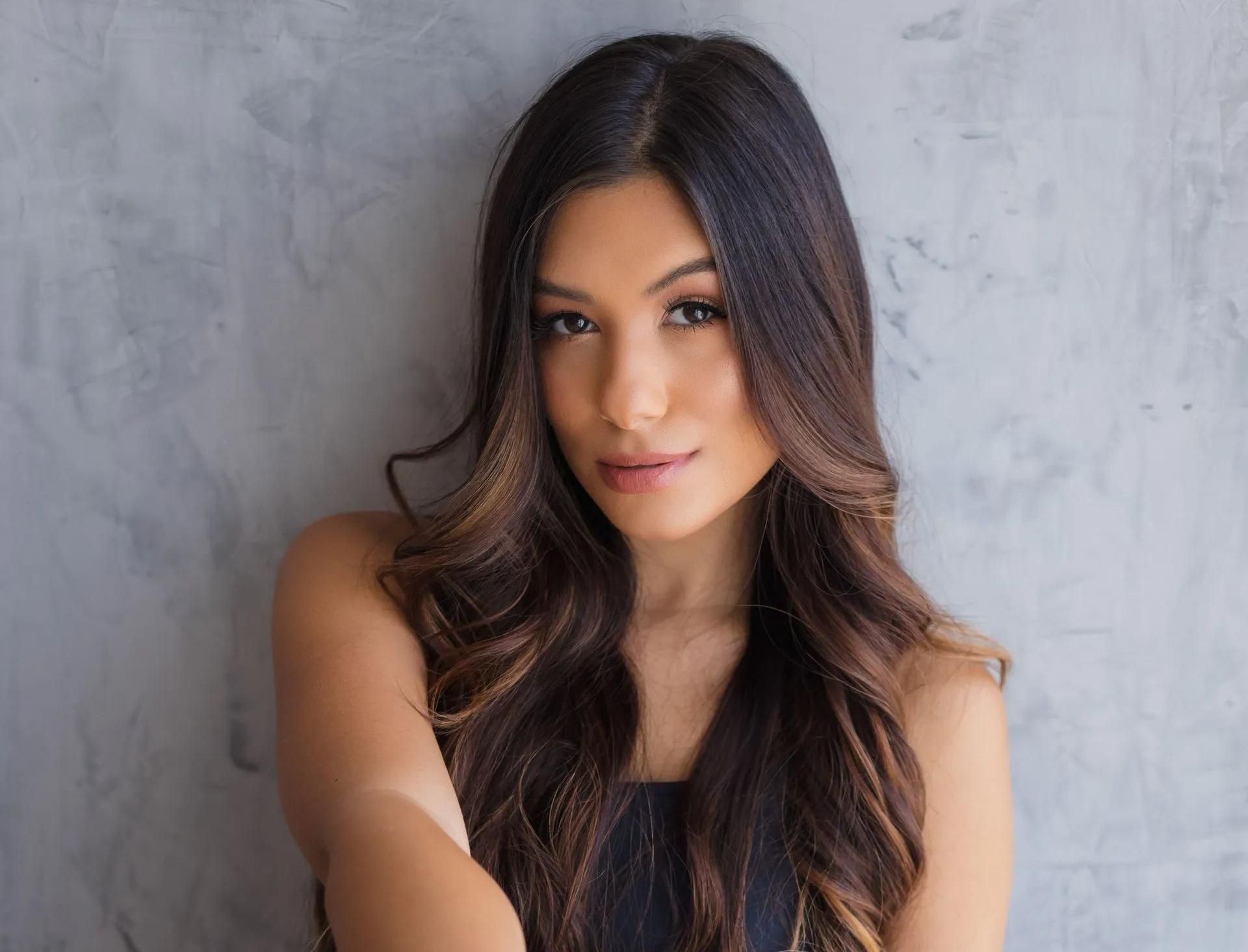 A Woman With Long Hair is Standing in Front of a Wall and Looking at the Camera — Southside Hair & Beauty Design In South Tamworth, NSW A Woman With Long Hair is Standing in Front of a Wall — Southside Hair & Beauty Design In South Tamworth, NSW