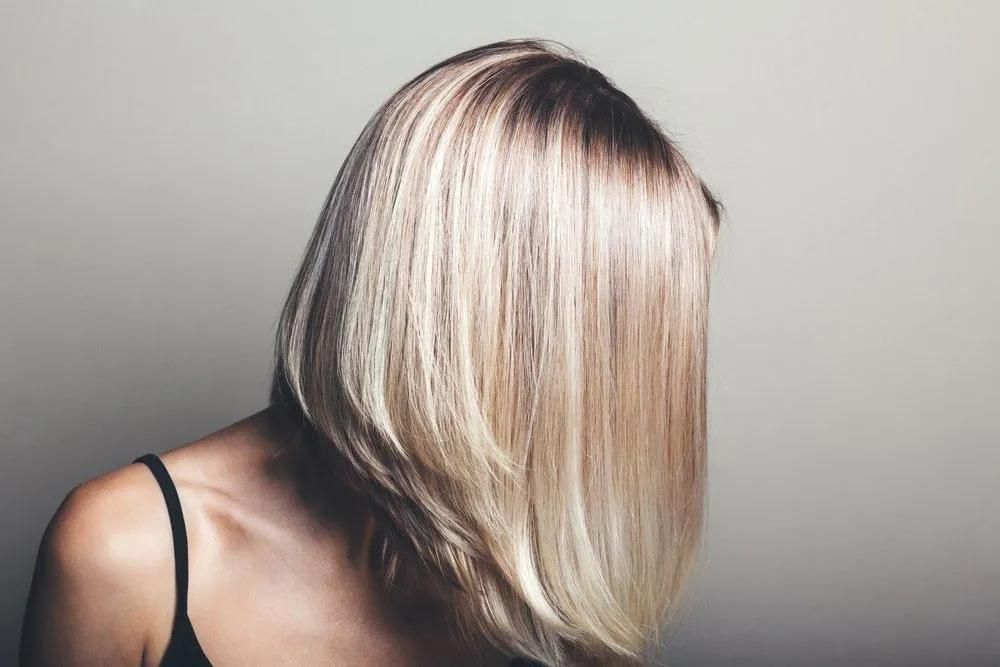 A Woman With Blonde Hair is Covering Her Face With Her Hair — Southside Hair & Beauty Design In South Tamworth, NSW