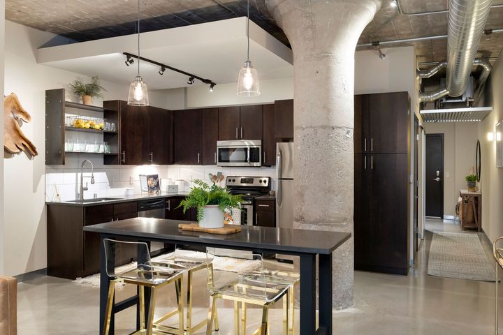 A large floor plan showcasing a dining area and modern kitchen with dark cabinets and stainless steel appliances set against polished concrete floors and concrete walls.