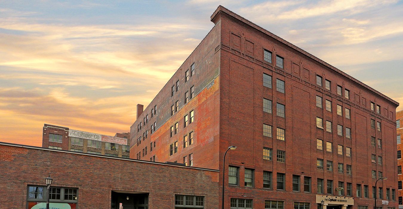A multi-story red brick warehouse building stands against a sunset sky.