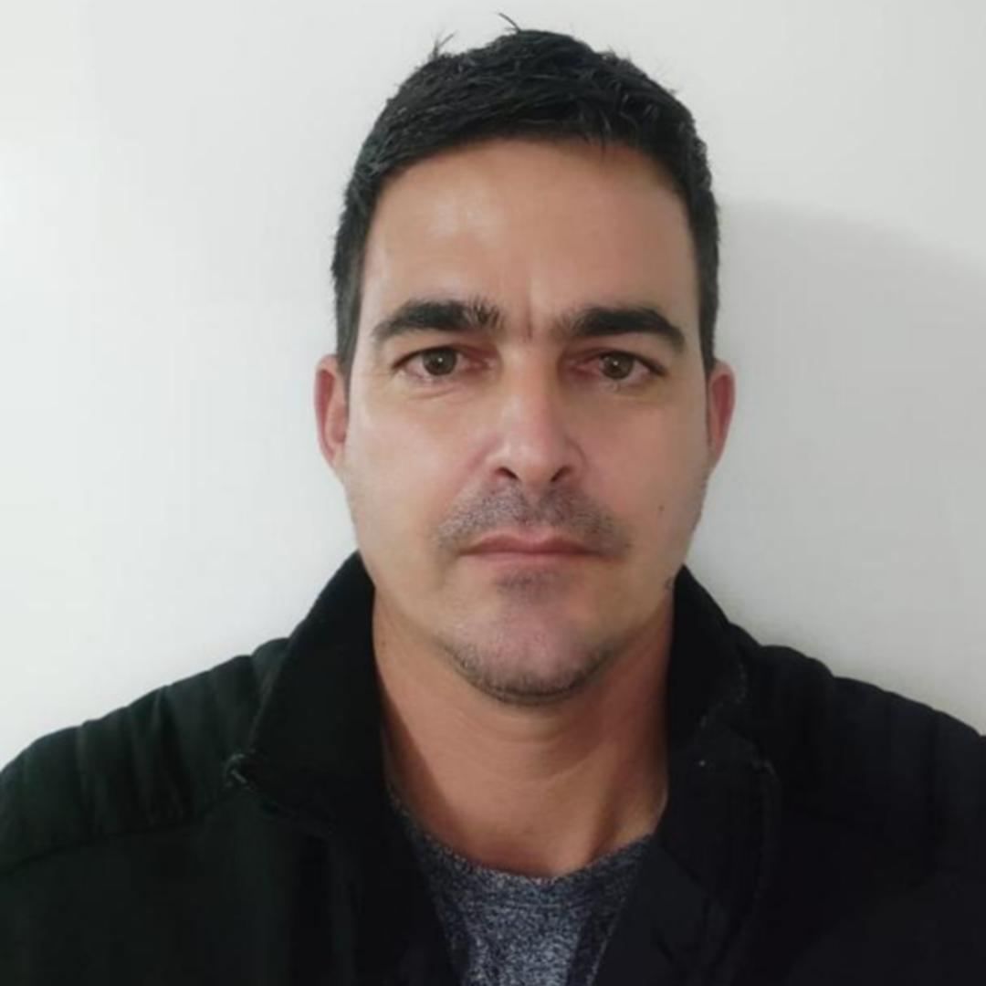 Un hombre con barba lleva una chaqueta negra y una camisa gris.