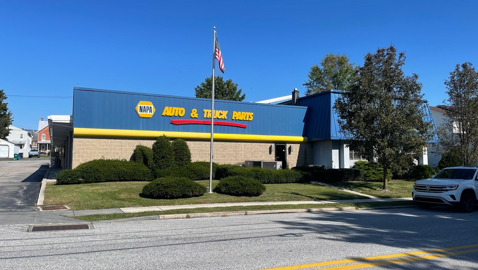 Blue and yellow NAPA Auto & Truck Parts store with an American flag on a sunny day.