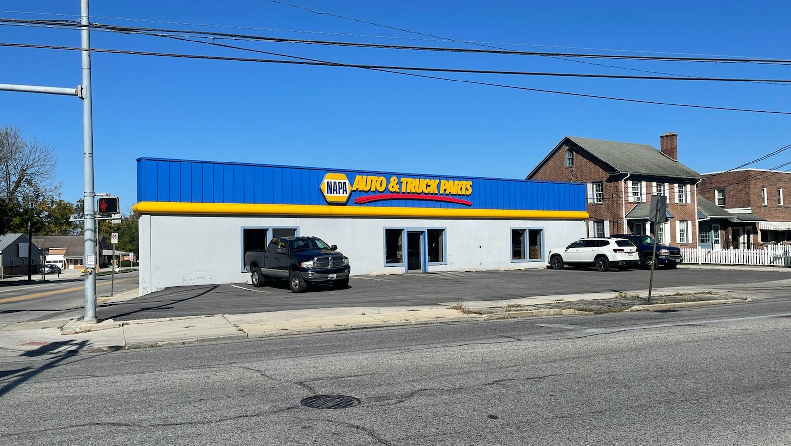 NAPA Auto Parts store with blue and yellow signage. Two trucks parked outside on a sunny day.