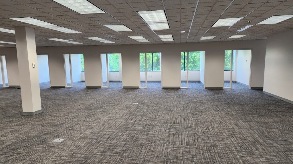 A large empty office with a carpeted floor and a lot of windows.