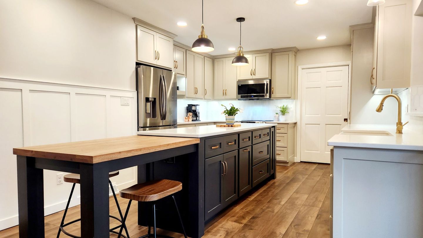 A kitchen with white cabinets , stainless steel appliances , a large island and a wooden table.