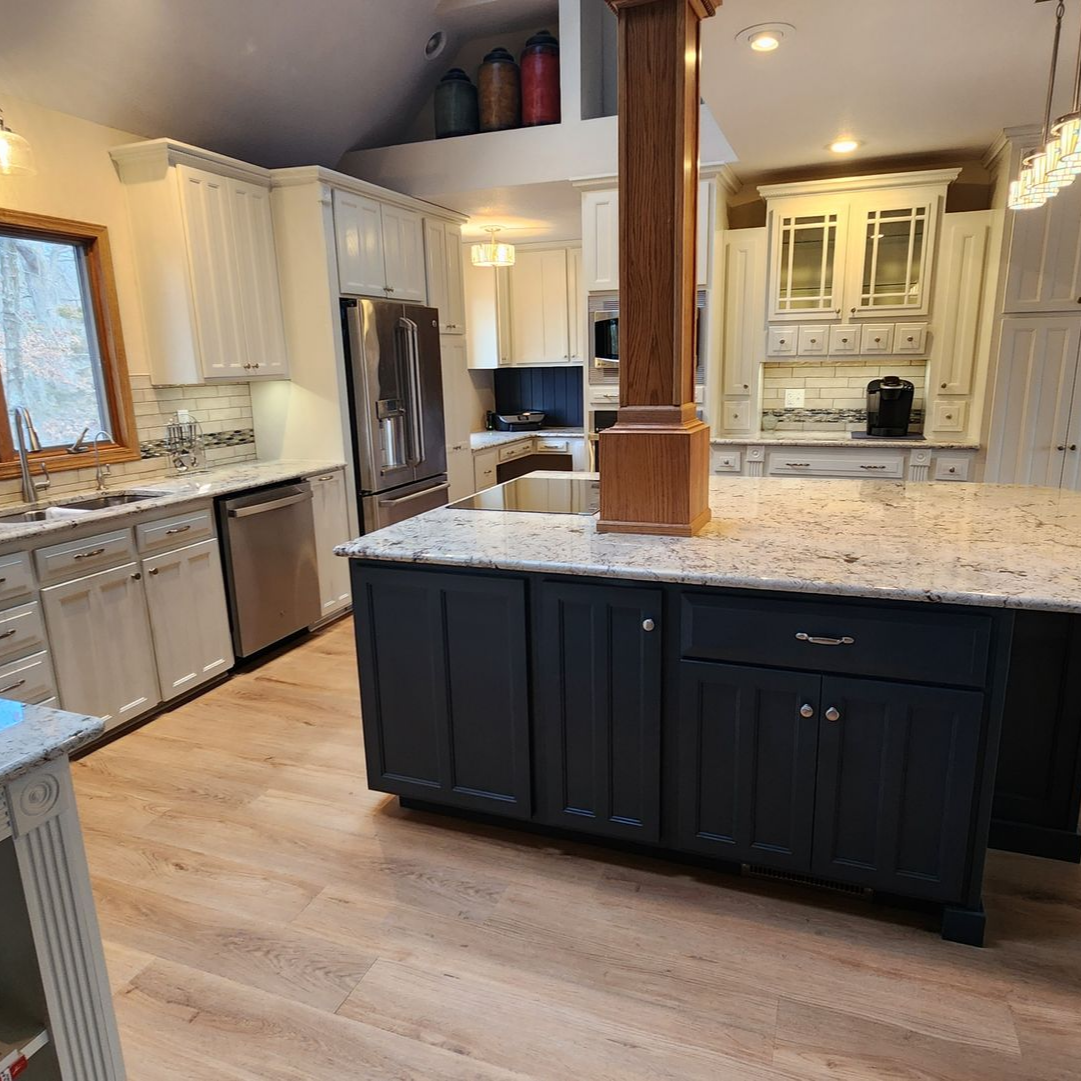 Kitchen with dark blue island, white cabinets, stainless steel appliances, and wooden floors.