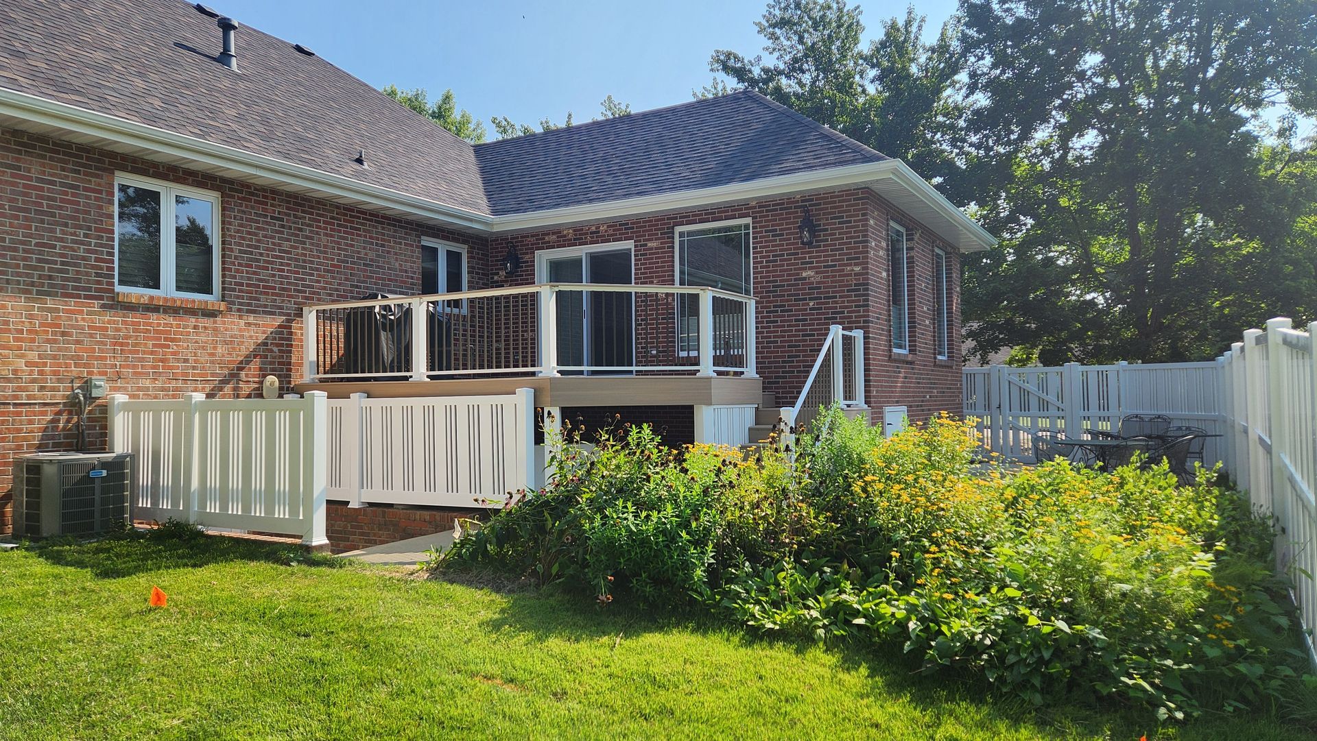 The backyard of a brick house with a deck and a white fence.