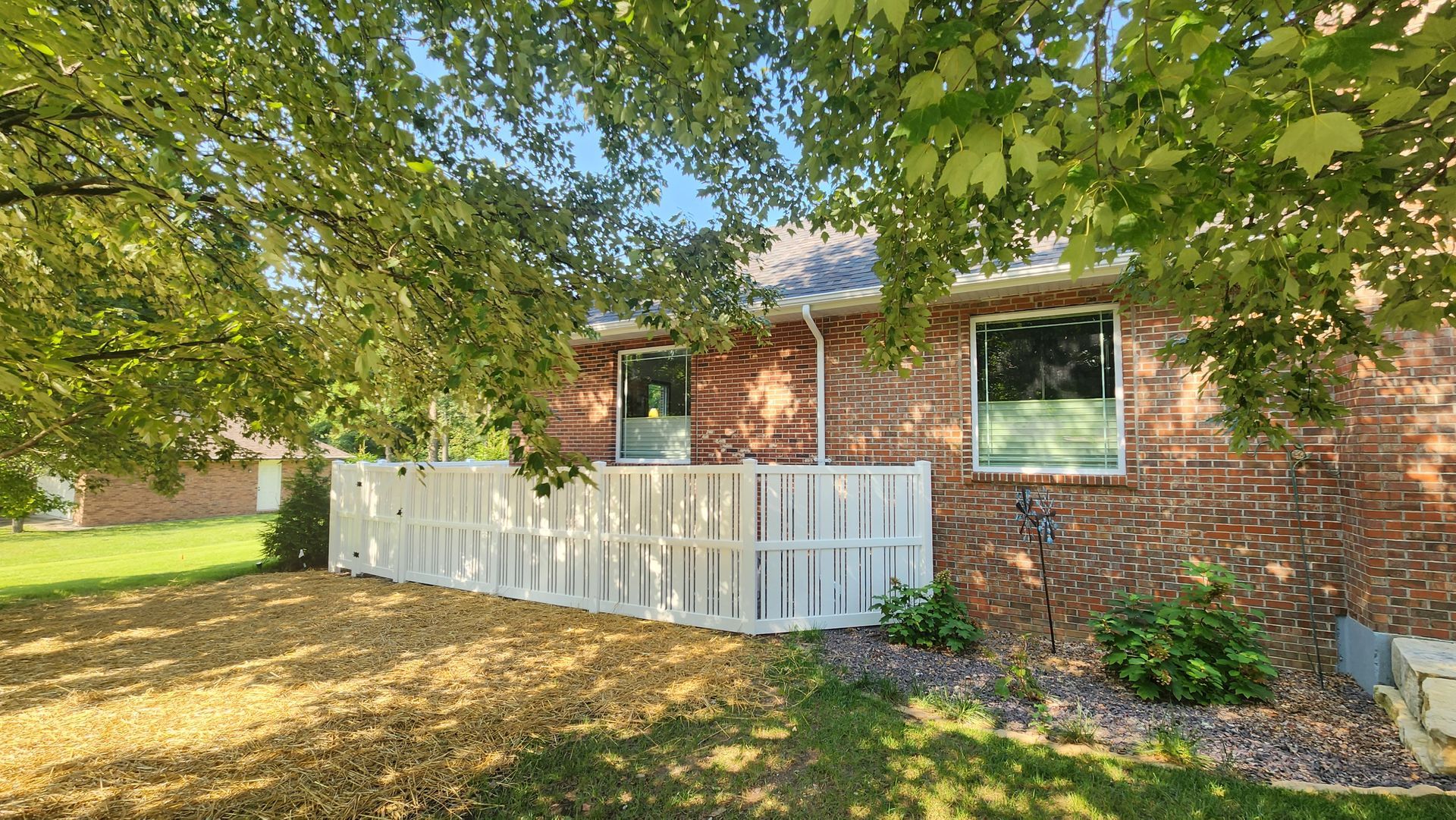 A brick house with a white fence and a tree in front of it.
