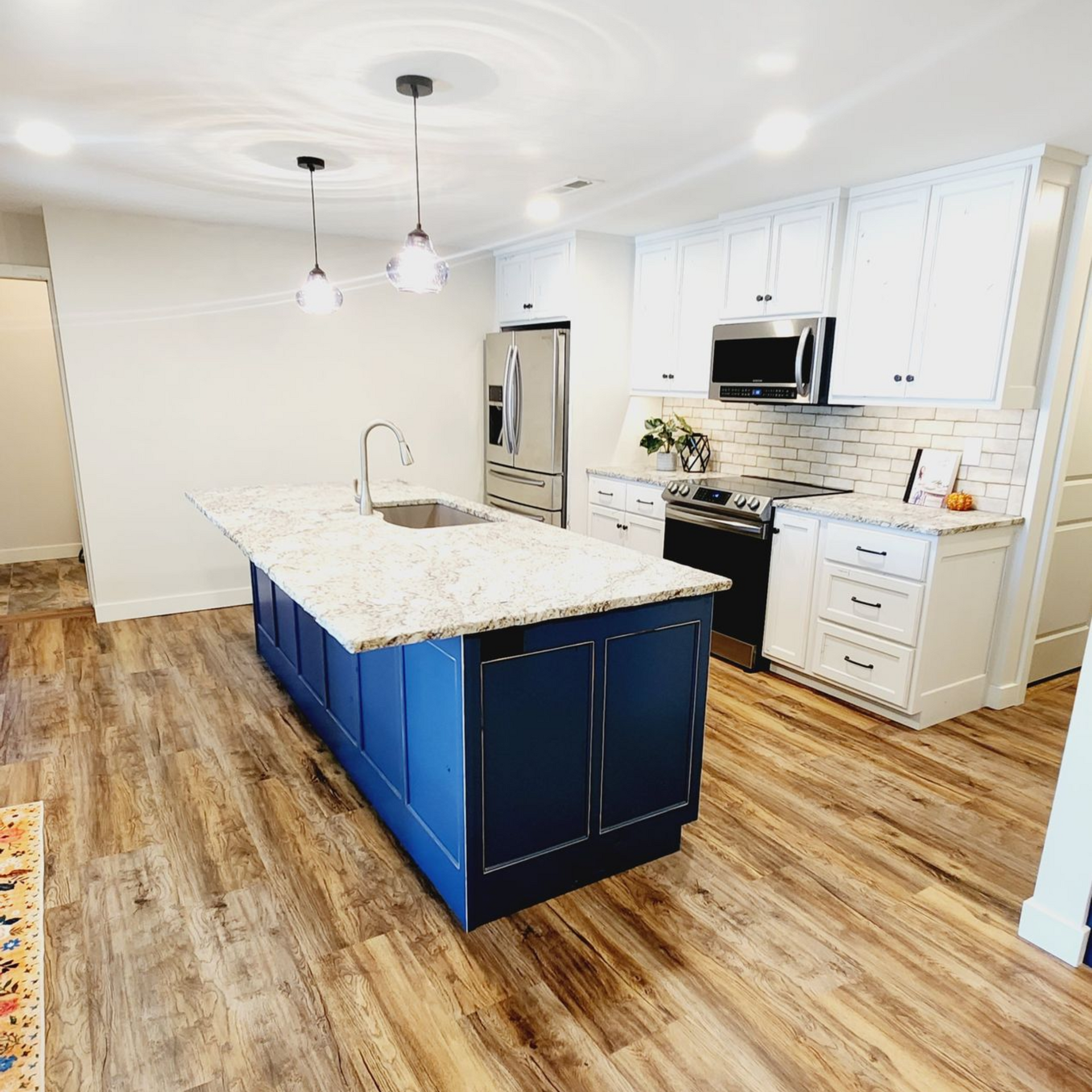 Modern kitchen with blue island, white cabinets, stainless steel appliances, and wood floors.