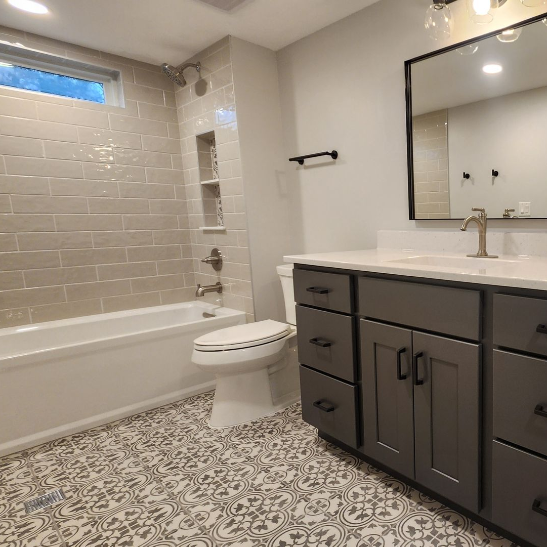 Bathroom with tiled shower/tub, gray vanity, patterned floor, and large mirror.