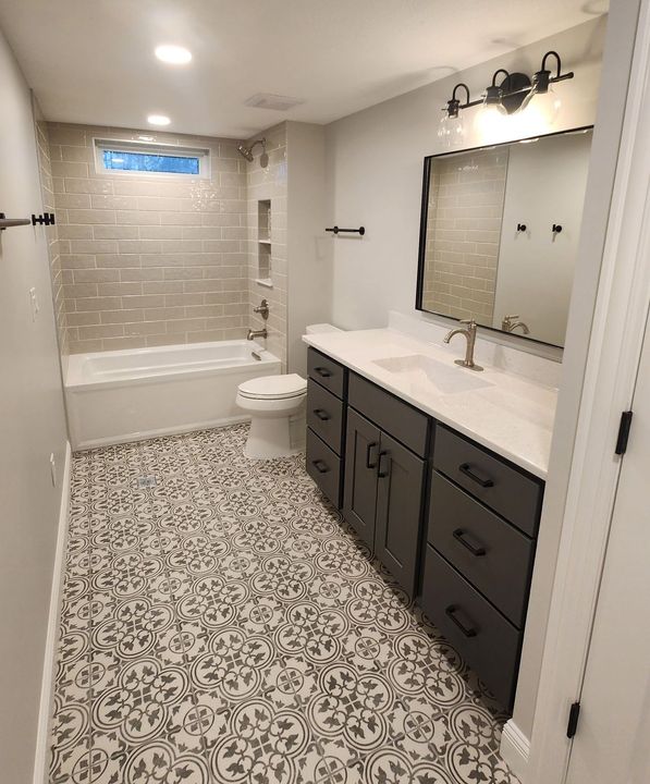 A bathroom with a walk in shower , sink , mirror and blue cabinets.