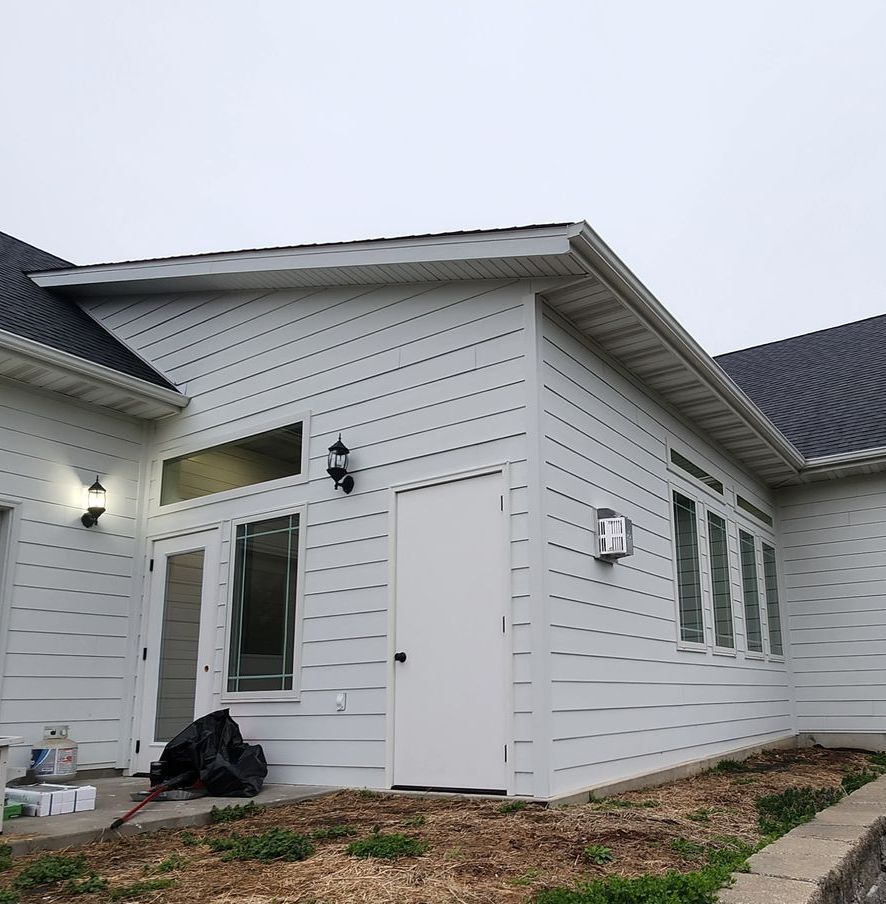 White-sided house extension with door, windows, and dark roof against a cloudy sky.