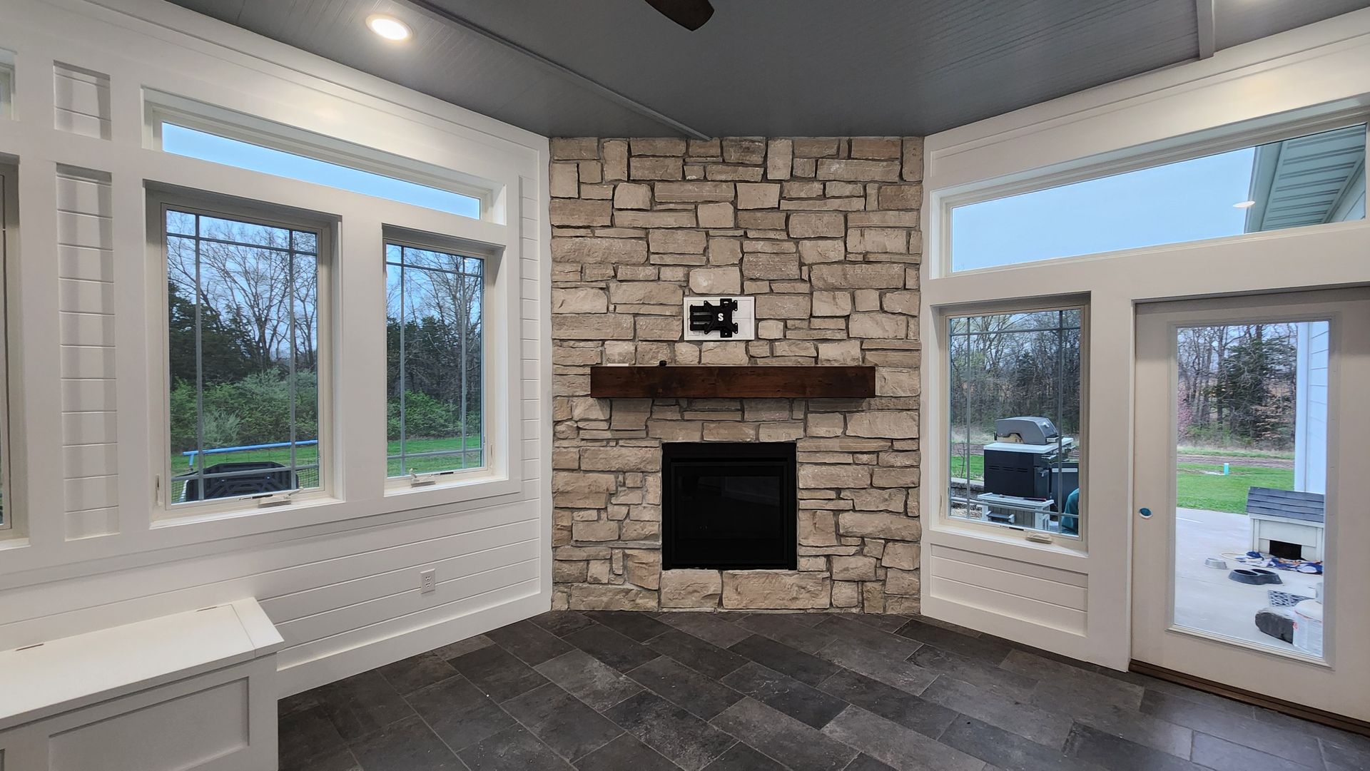 Interior room with stone fireplace, windows, and dark wood flooring.