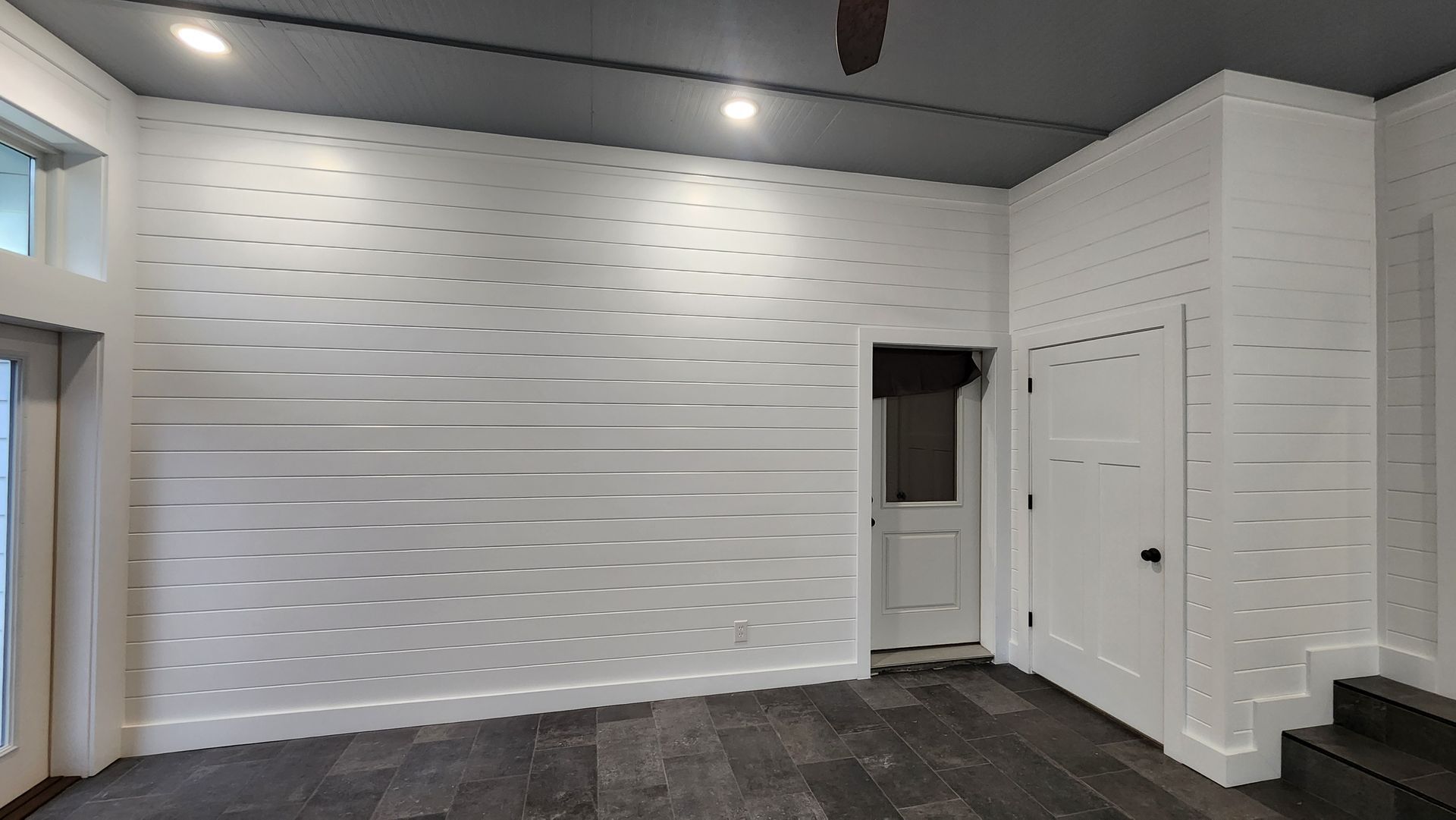 White-walled room with dark wood floor, small white door, and overhead lighting.