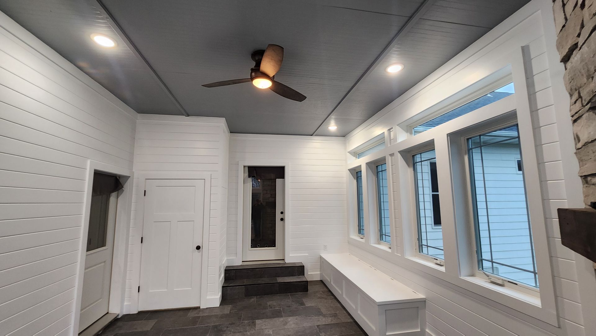 Sunroom with white walls, gray ceiling, windows, built-in bench, and a ceiling fan.