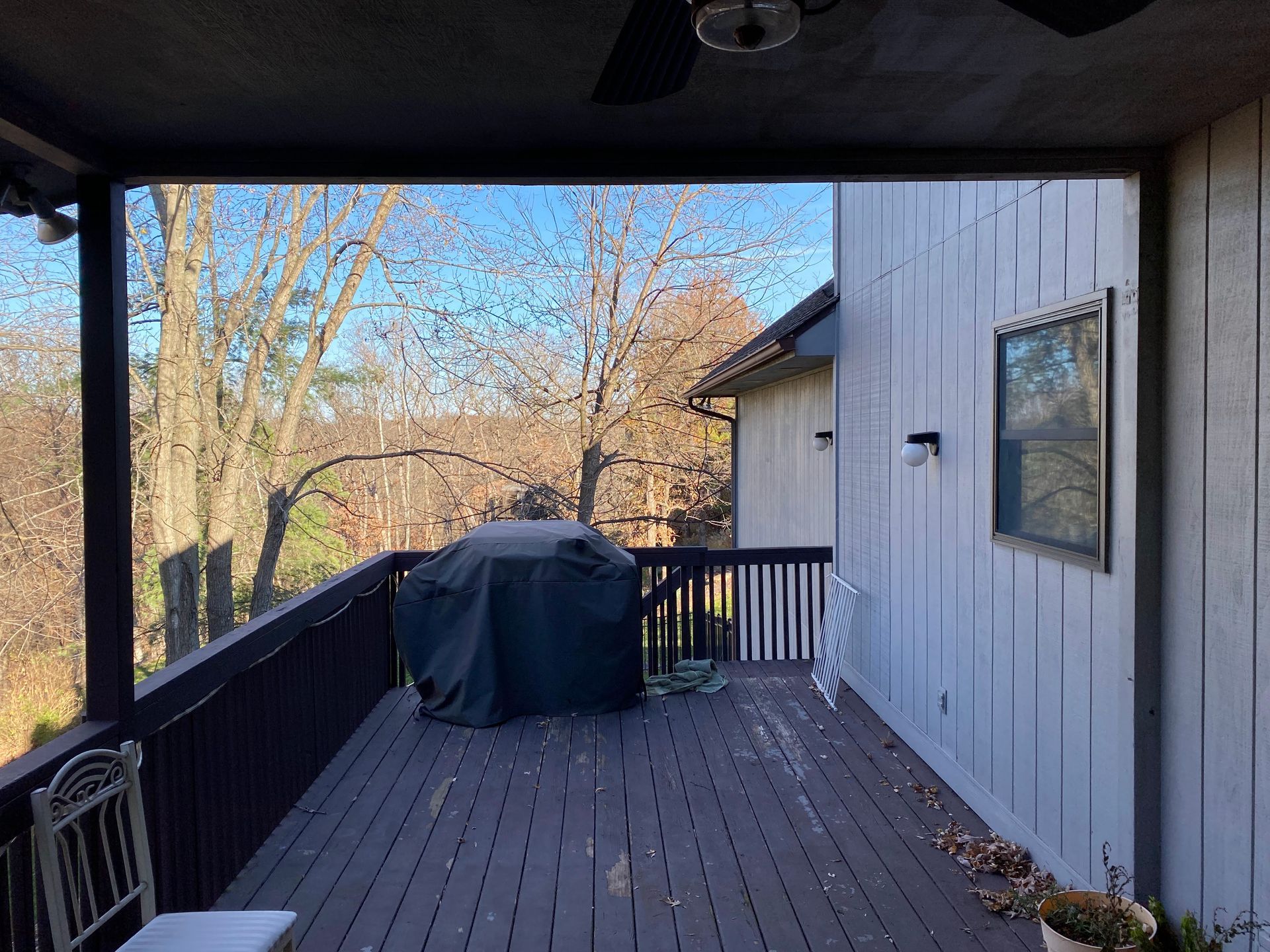 Wooden deck with grill and chair, next to a white house with a blue sky background.