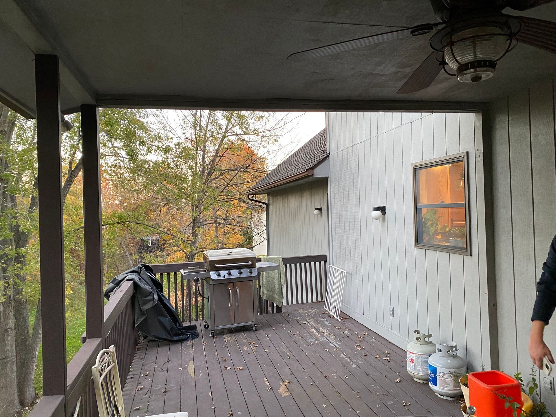 Covered porch with grill, propane tanks, and a view of trees.