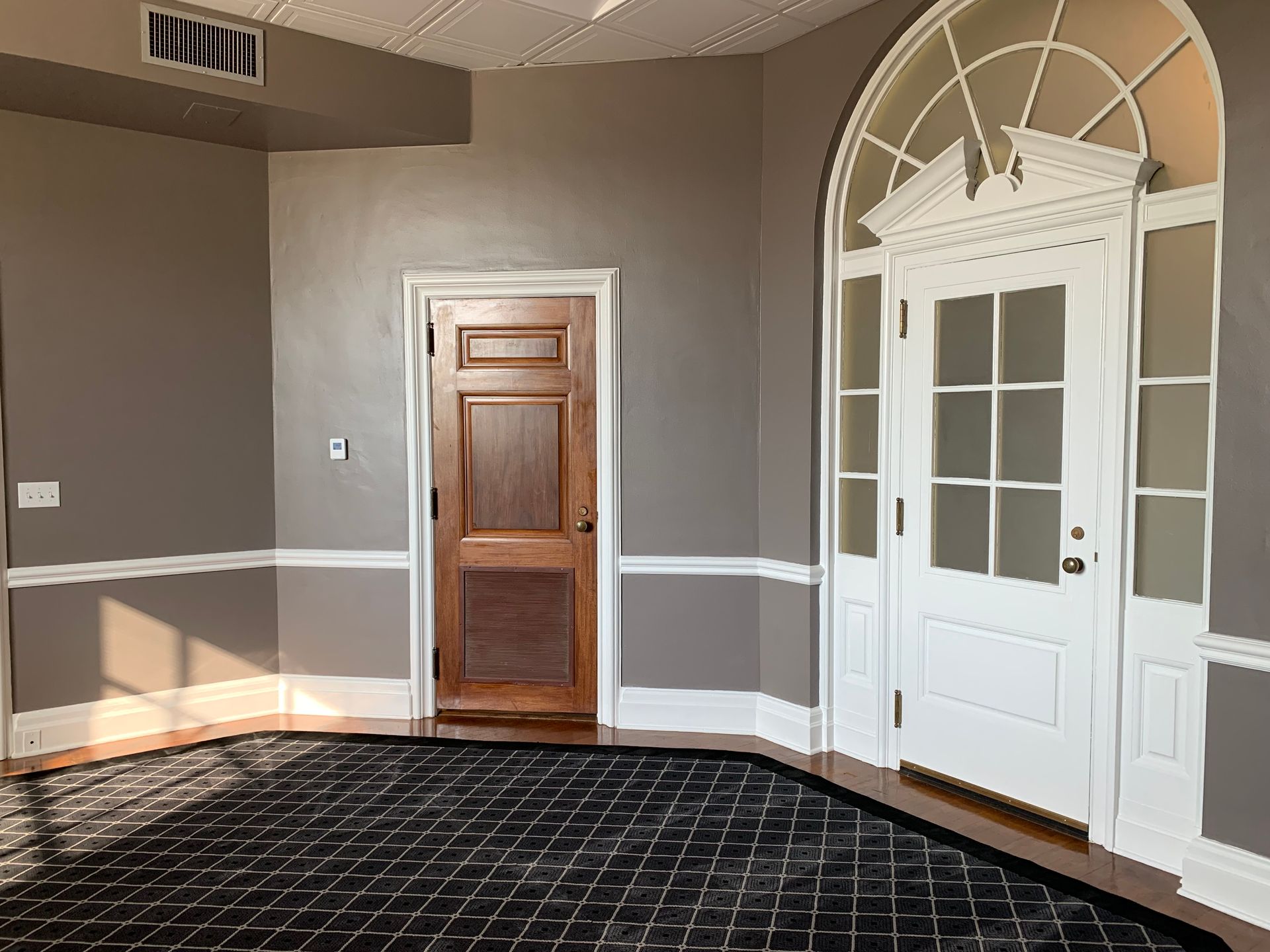 An empty room with a wooden door and a white door.