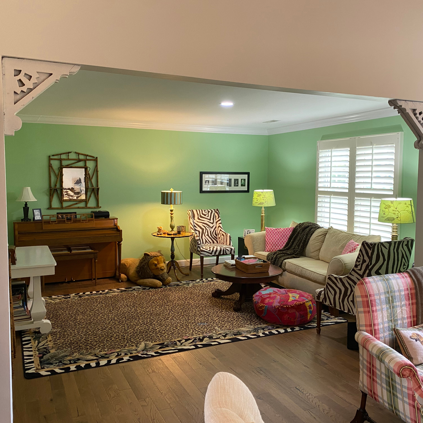 Living room with green walls, piano, sofa, zebra print chairs, and animal print rug.