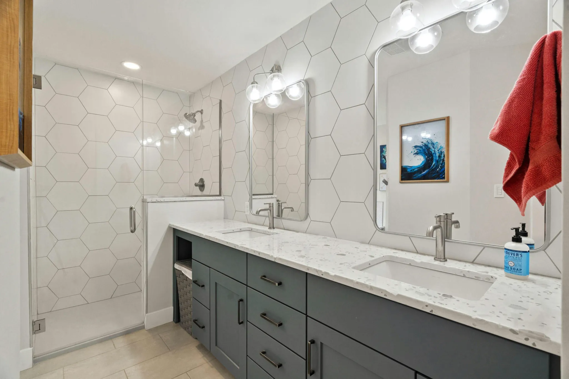 A bathroom with a walk in shower , sink , mirror and blue cabinets.