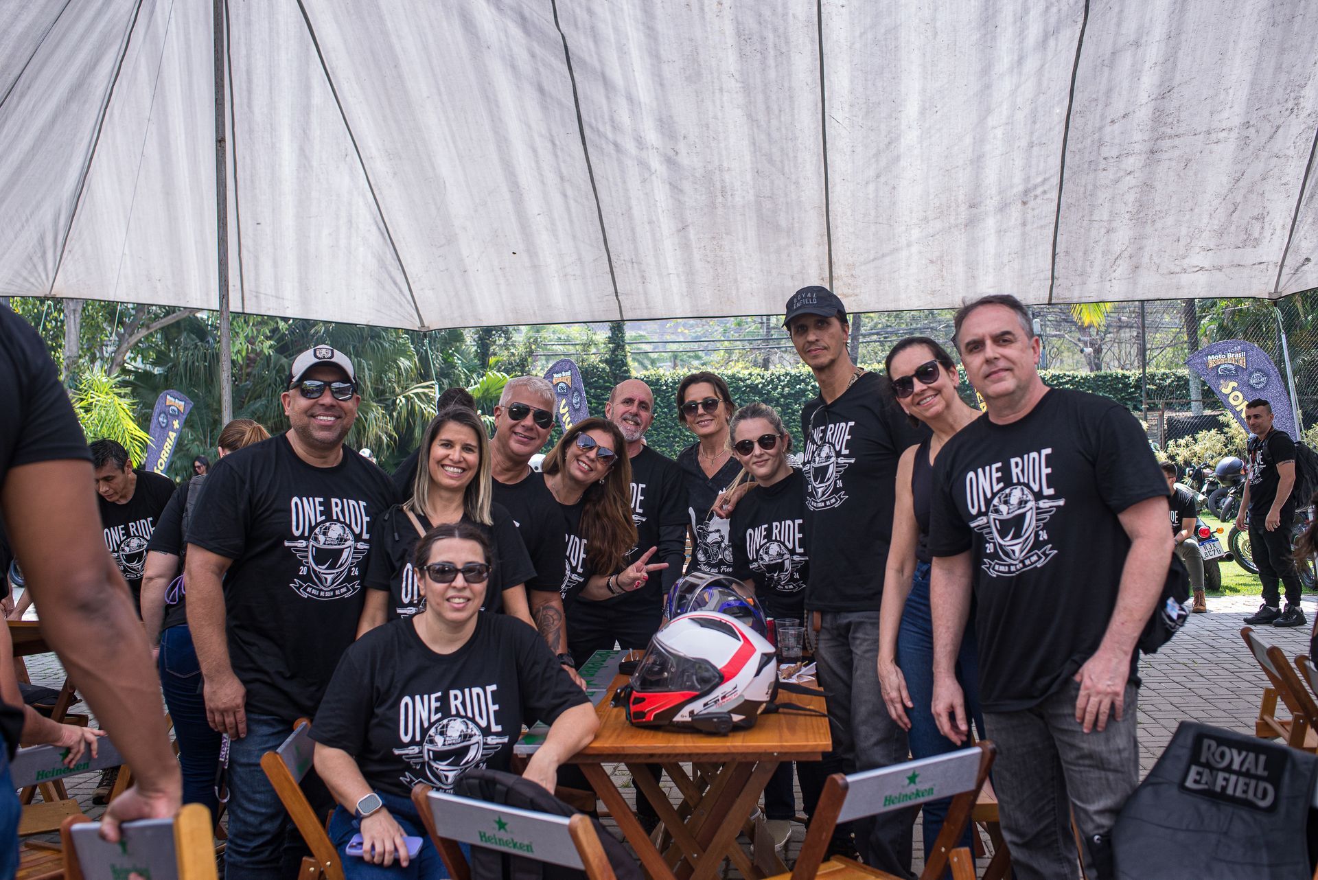 Grupo de pessoas vestindo camisetas pretas posando sob uma tenda em um evento ao ar livre.