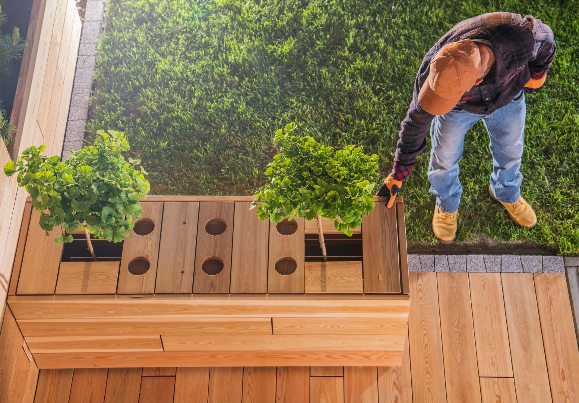 A man is standing on a wooden deck next to a wooden box filled with plants.