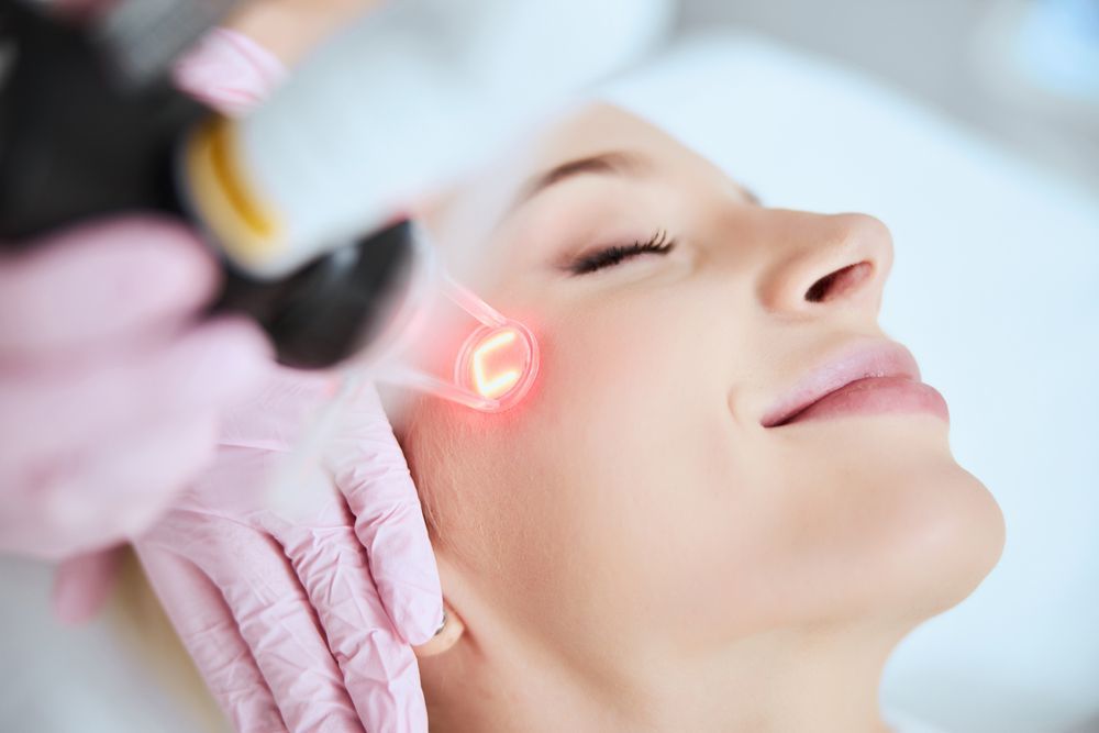 Close-up of a person’s face as a gloved finger presses a cheek, likely during a skincare treatment.