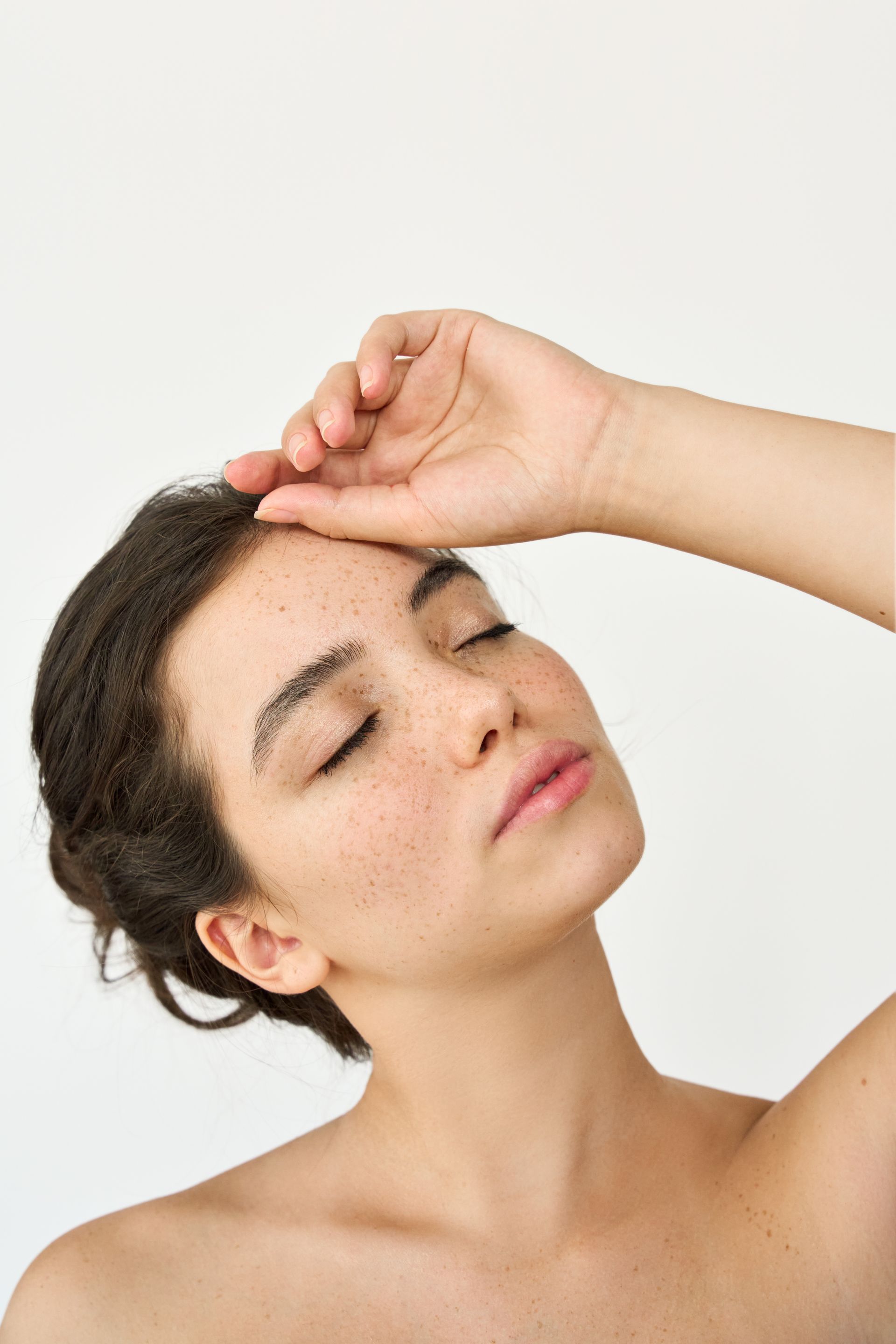 Woman with closed eyes, hand on forehead, against white background.