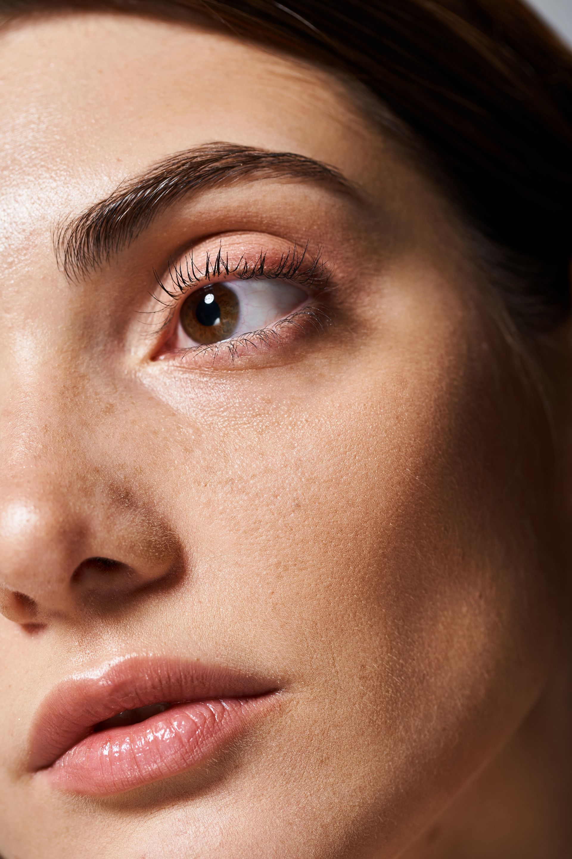 Close-up of a person looking upwards, featuring prominent eyebrows and shimmering skin.