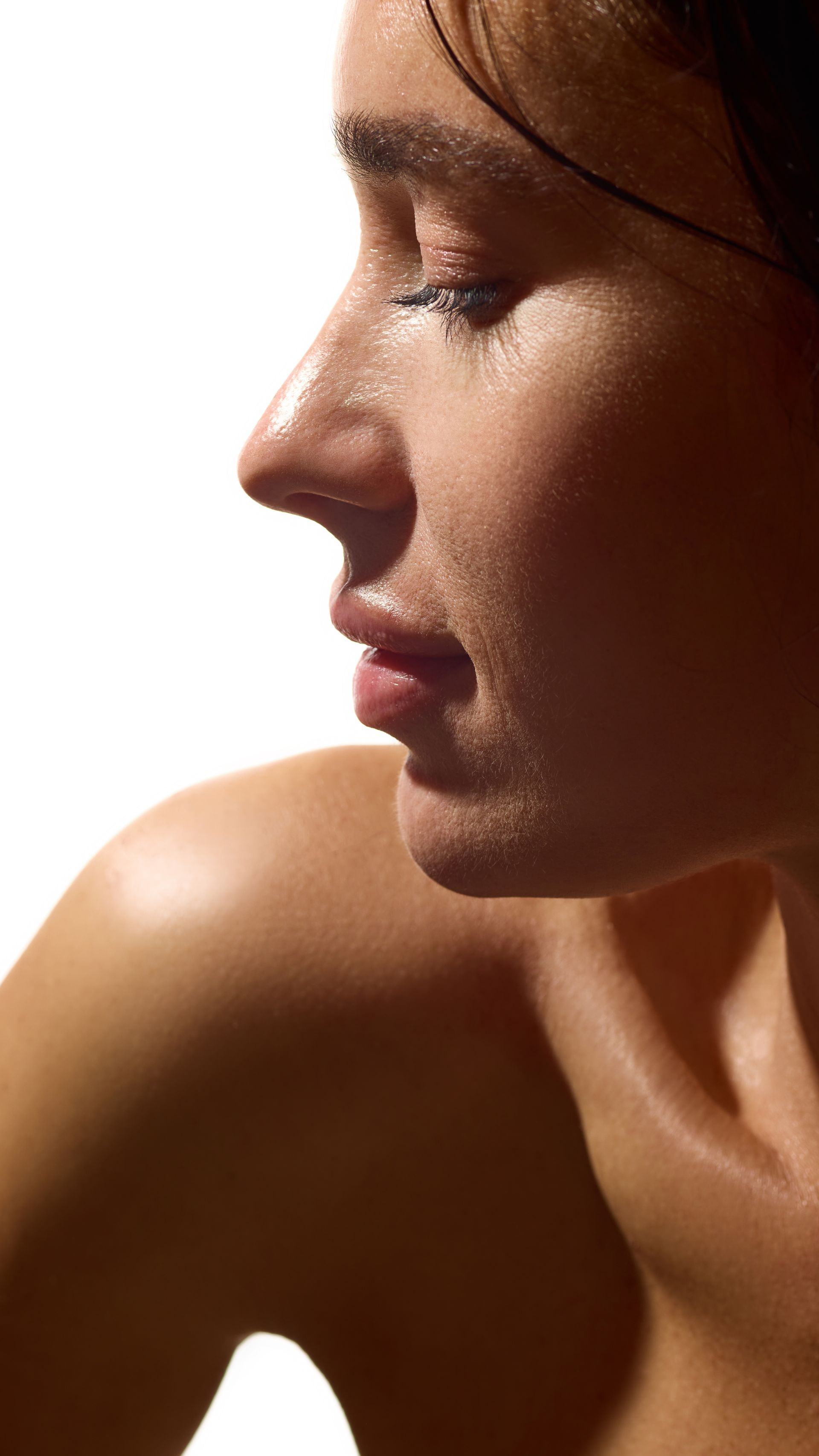 Profile of a person with glowing skin; eyes closed, slight smile. Shoulder and neck visible. Bright lighting.
