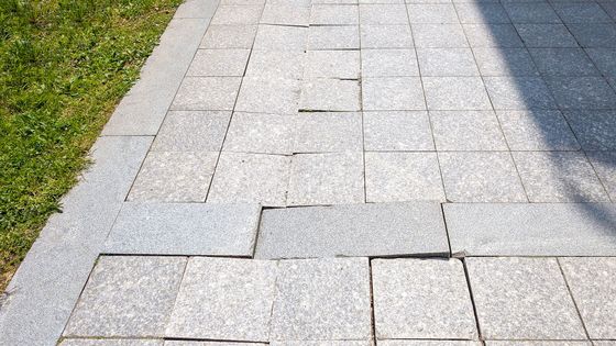 Backyard patio with stacked concrete pavers, a storage bin, hoses, and a stucco wall.