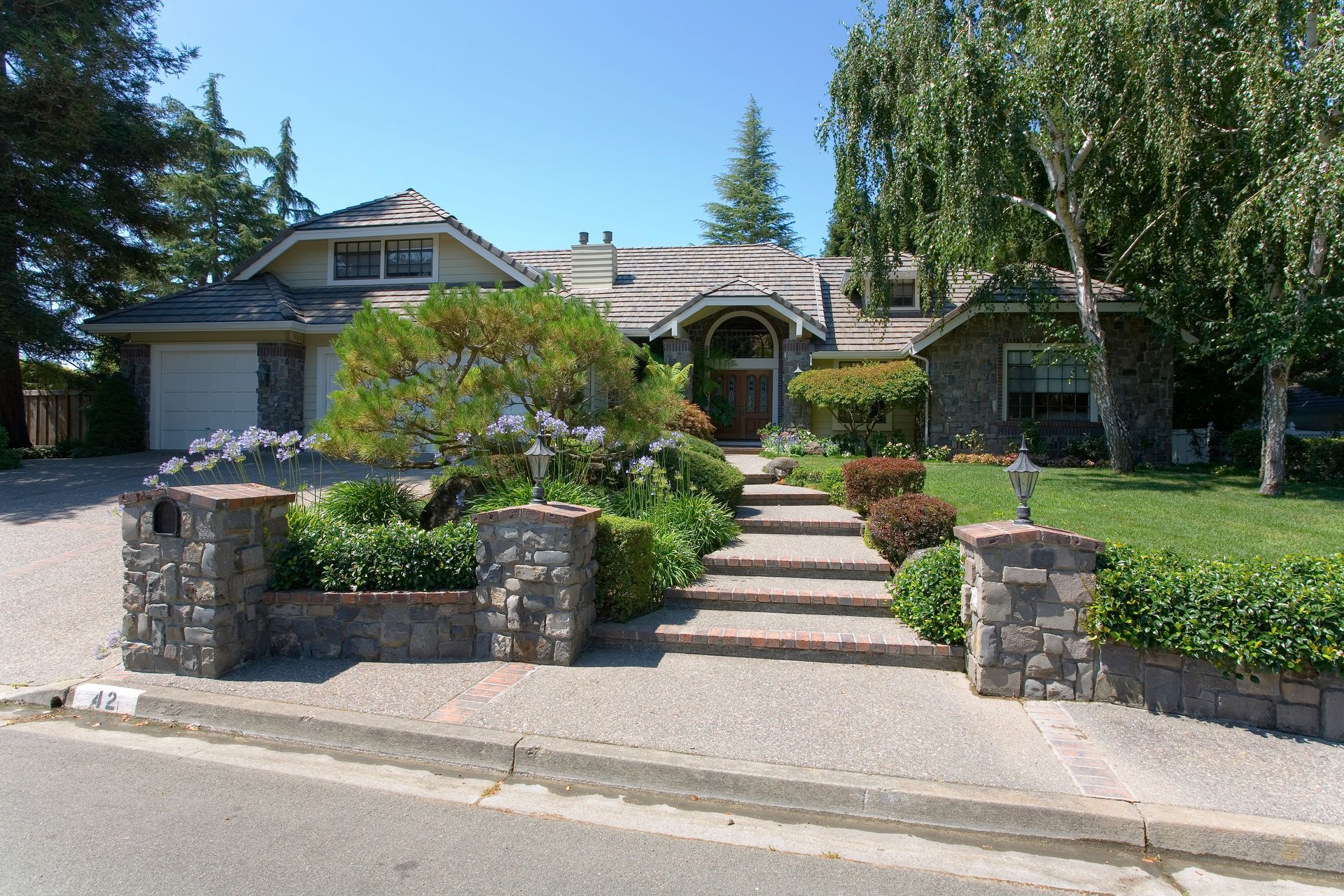 Suburban house with stone gateposts, landscaped front yard, and walkway leading to the entrance