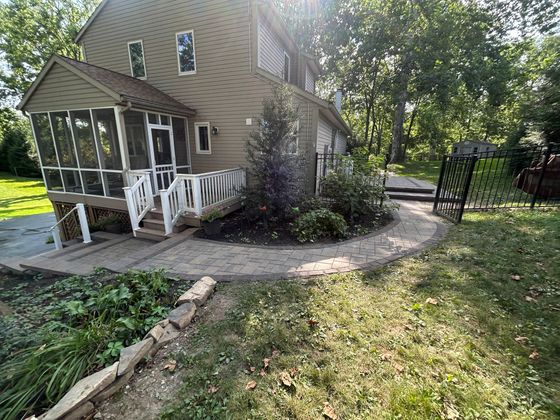 House with screened porch, curved stone walkway, and landscaped yard in a wooded setting