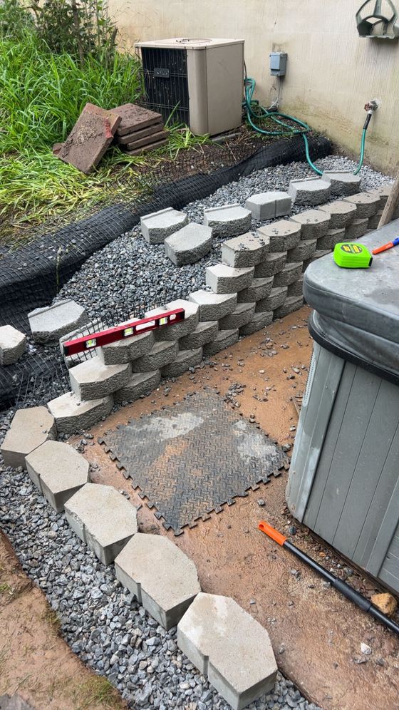 Backyard with a stone pathway, gravel borders, pavers, and a trash bin beside a wall