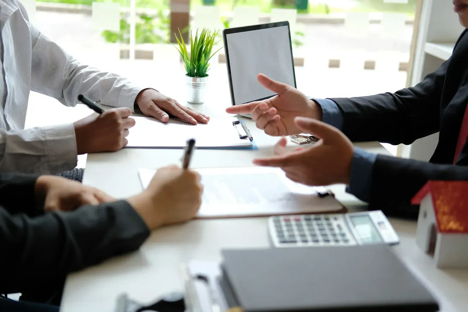 People in a meeting discussing documents around a desk with a tablet and notebook