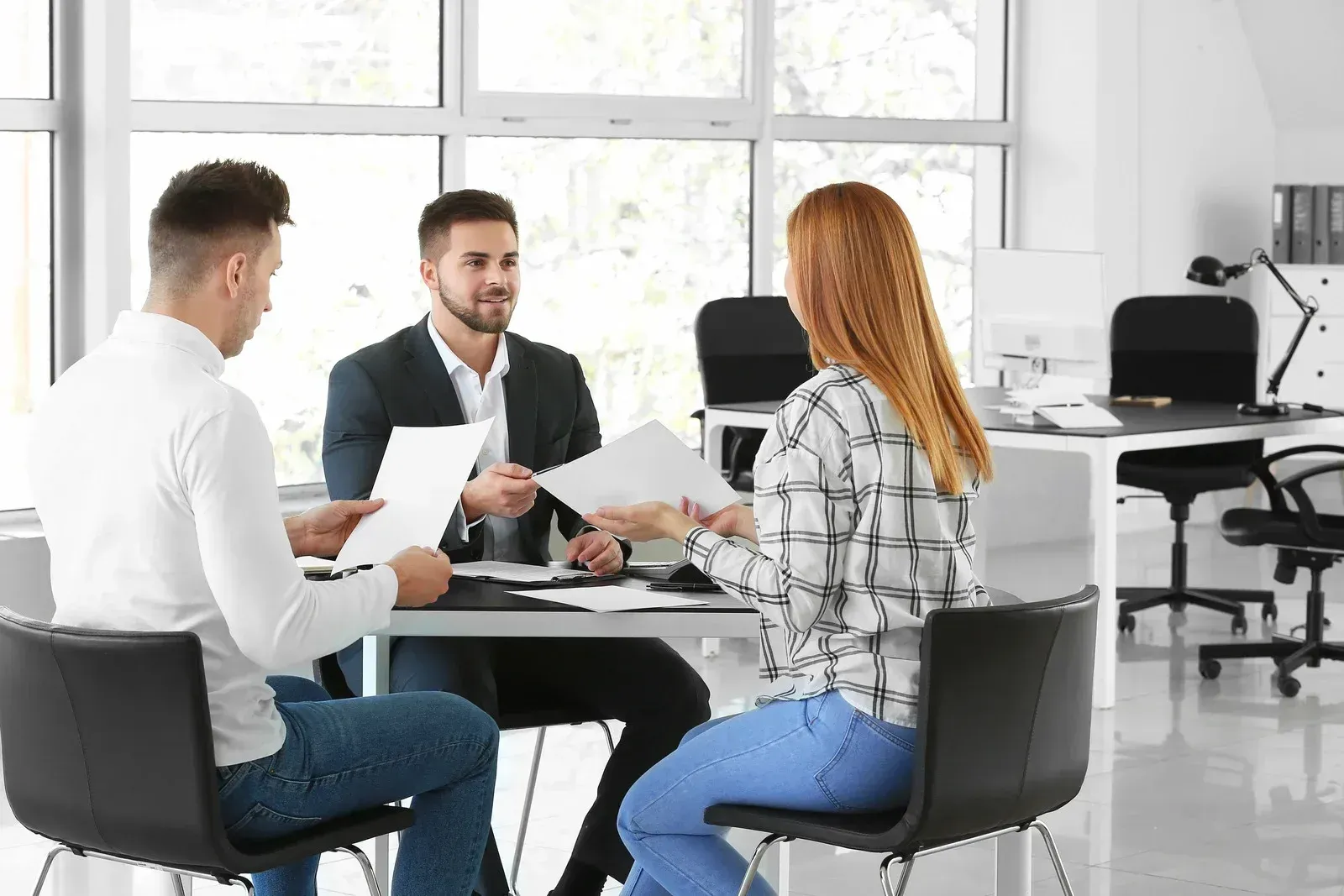 Three coworkers discussing documents around a table in a bright office