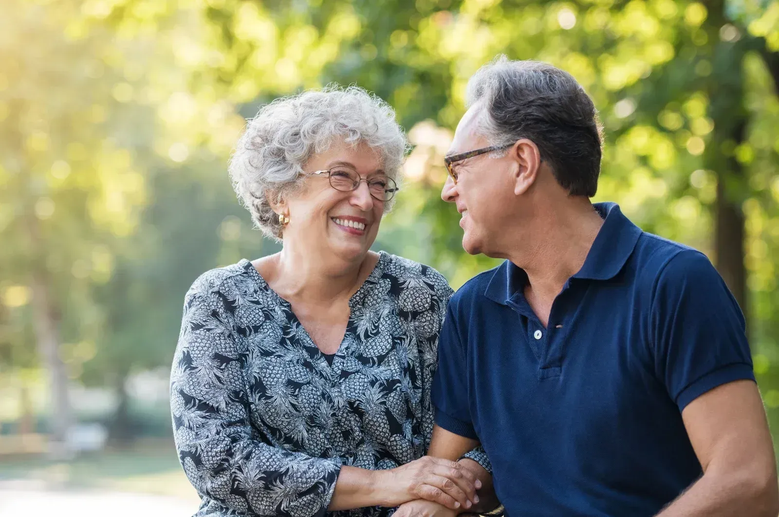 Two smiling people sitting outdoors, holding hands and talking in a sunny park