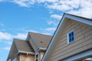 Beige house with gabled roof, blue window, and cloudy sky background.