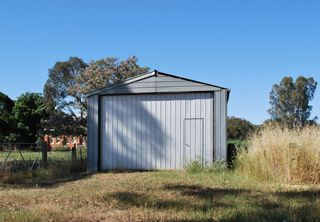 Metal shed in a grassy field with a small door, under a clear blue sky.