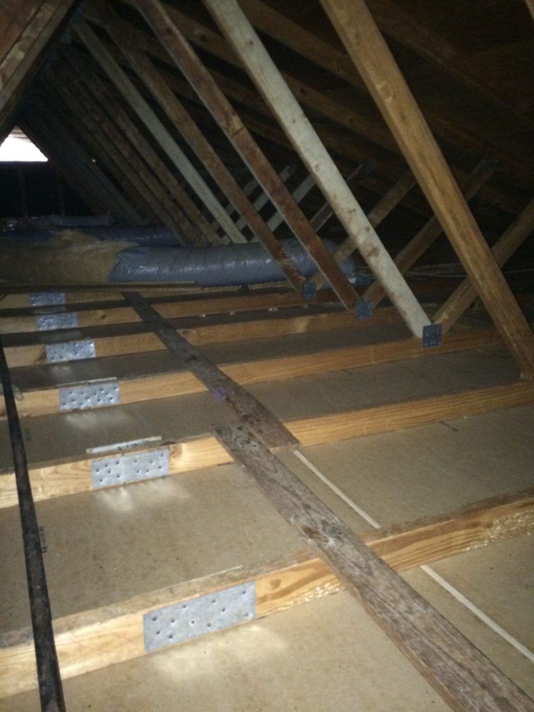 View of an attic with wooden rafters and a partially visible window at the apex.