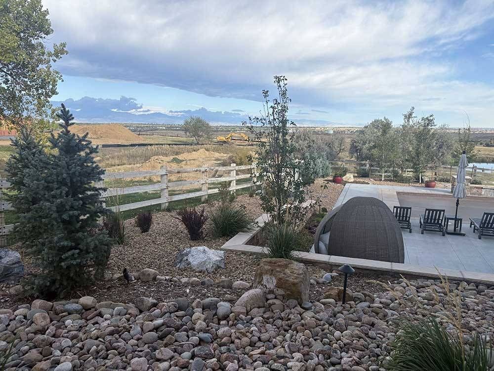 A desert-style backyard with stone landscaping, a white fence, an igloo-shaped chair, and mountain views.